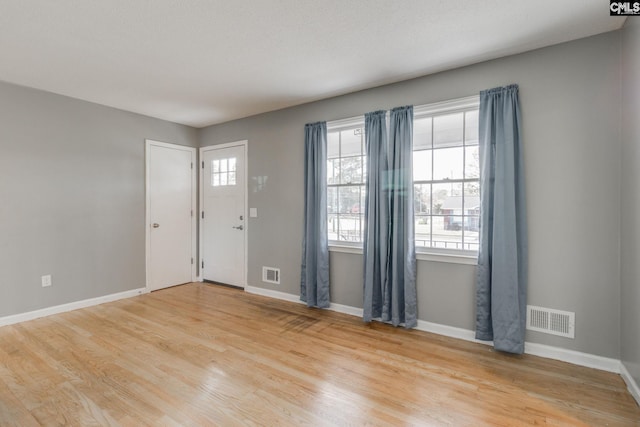 foyer entrance with light wood finished floors, baseboards, and visible vents