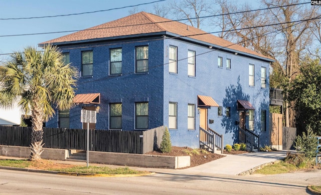 view of front facade with entry steps, brick siding, and fence