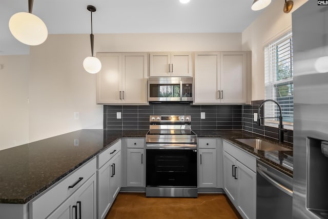 kitchen featuring stainless steel appliances, a peninsula, a sink, hanging light fixtures, and decorative backsplash