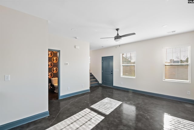 spare room with finished concrete flooring, visible vents, stairway, ceiling fan, and baseboards