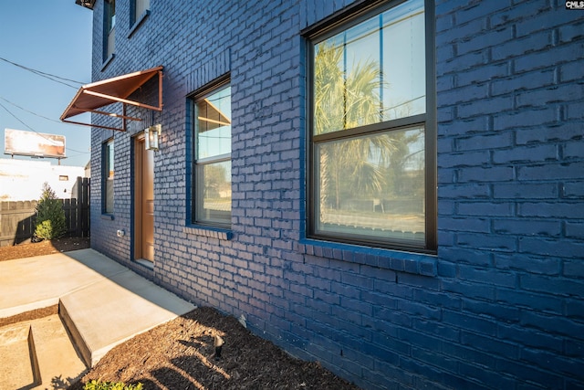 view of property exterior featuring brick siding, fence, and a patio