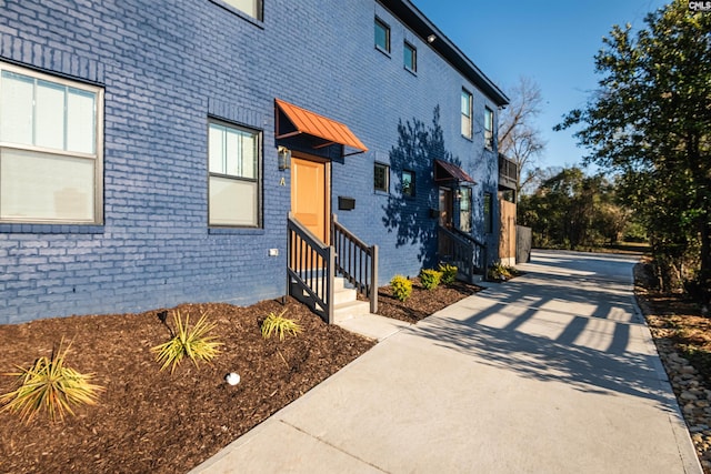 exterior space featuring entry steps, a standing seam roof, brick siding, and metal roof