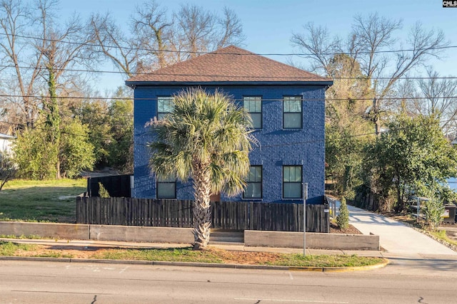 view of property exterior with a fenced front yard, roof with shingles, and brick siding