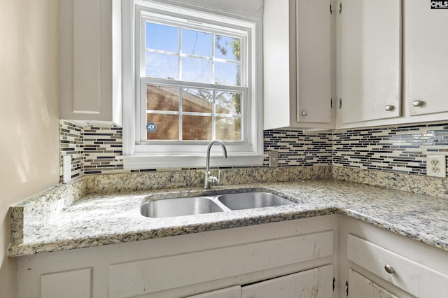 kitchen featuring light stone counters, backsplash, a sink, and white cabinets