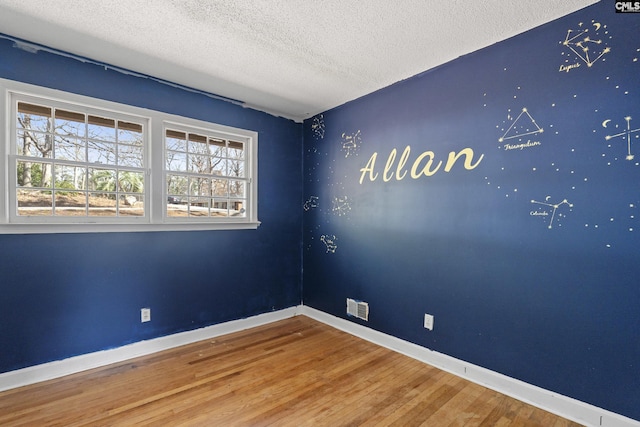 spare room featuring a textured ceiling, an accent wall, wood finished floors, visible vents, and baseboards