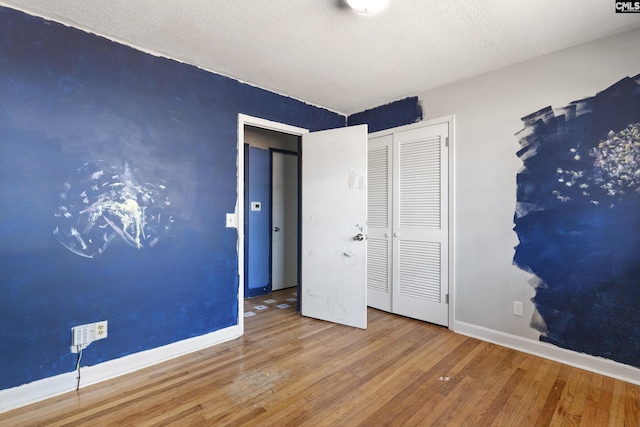 unfurnished bedroom with a textured ceiling, a closet, baseboards, and wood finished floors