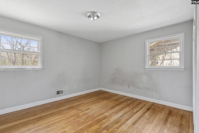 empty room with light wood-style floors, baseboards, visible vents, and a wealth of natural light