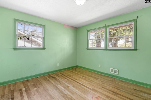 empty room with visible vents, a textured ceiling, baseboards, and wood finished floors