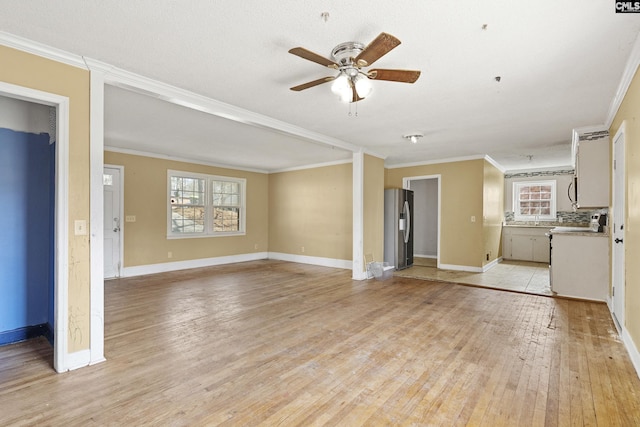 unfurnished living room with light wood finished floors, a ceiling fan, a wealth of natural light, and crown molding