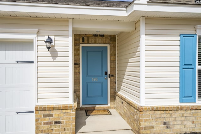 doorway to property with a garage and brick siding