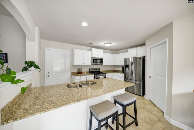 kitchen featuring appliances with stainless steel finishes, a peninsula, light stone countertops, white cabinetry, and a sink