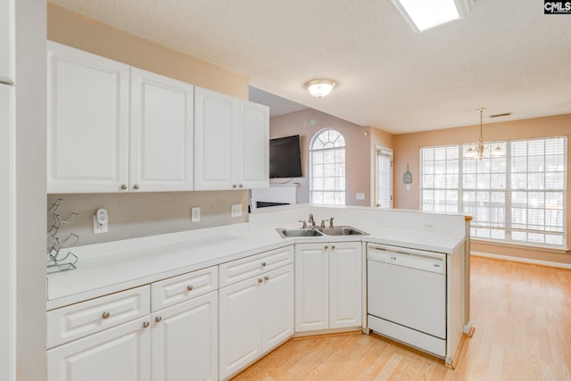 kitchen with white dishwasher, a peninsula, a sink, white cabinetry, and light countertops