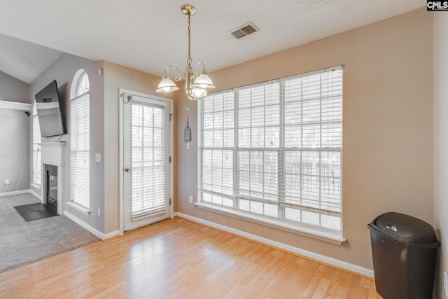 unfurnished dining area featuring a fireplace with flush hearth, visible vents, plenty of natural light, and wood finished floors