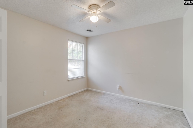 spare room with a textured ceiling, light carpet, visible vents, baseboards, and a ceiling fan