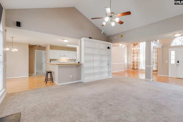 unfurnished living room featuring ceiling fan with notable chandelier, high vaulted ceiling, baseboards, and light colored carpet