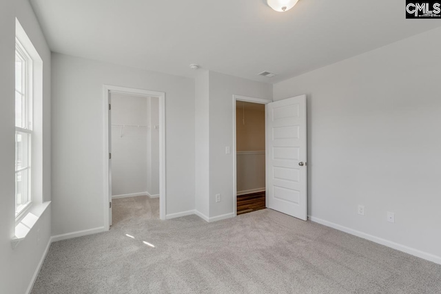 unfurnished bedroom with a closet, carpet flooring, a walk in closet, and baseboards