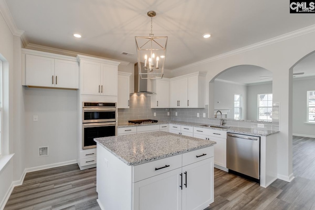 kitchen featuring crown molding, stainless steel appliances, tasteful backsplash, a sink, and wall chimney exhaust hood