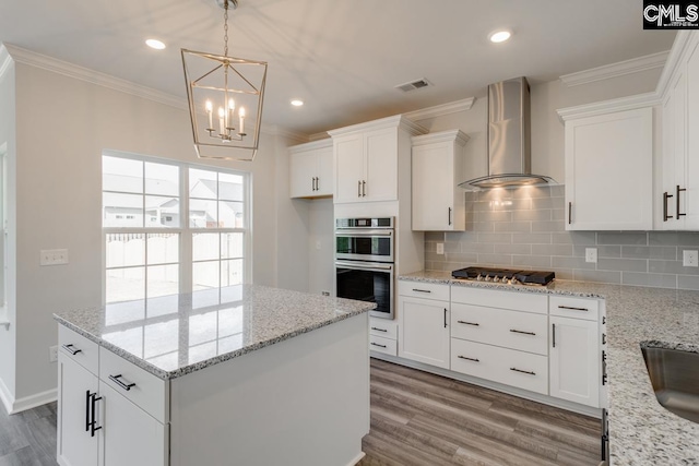 kitchen with white cabinetry, wall chimney range hood, appliances with stainless steel finishes, backsplash, and crown molding