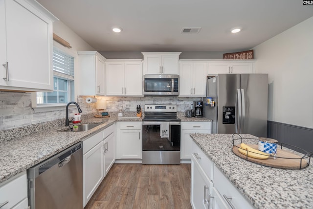 kitchen with stainless steel appliances, a sink, visible vents, white cabinetry, and light wood-type flooring