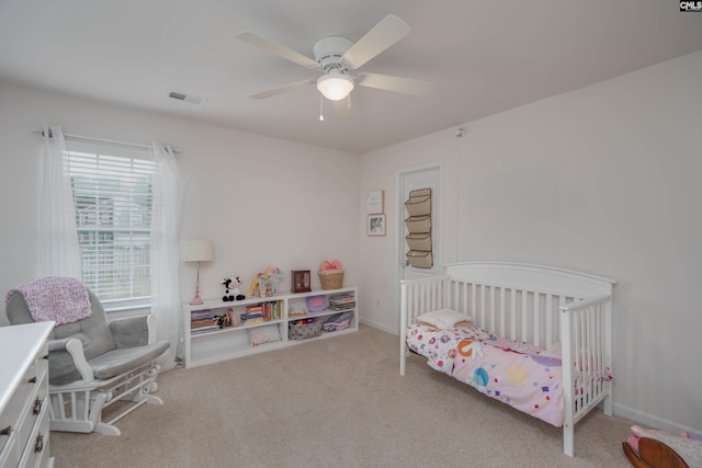 bedroom featuring carpet floors, a nursery area, ceiling fan, and visible vents