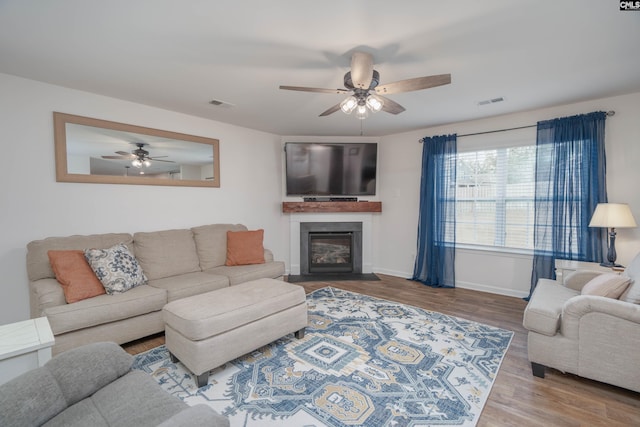 living area featuring visible vents, a fireplace with flush hearth, ceiling fan, wood finished floors, and baseboards