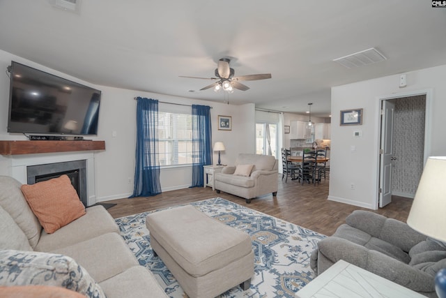 living room featuring a ceiling fan, a fireplace, visible vents, and wood finished floors