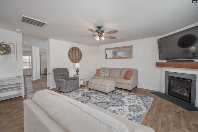 living room featuring visible vents, a glass covered fireplace, ceiling fan, wood finished floors, and baseboards