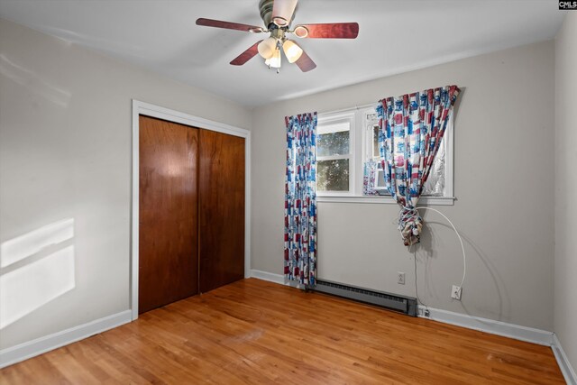 unfurnished bedroom with a closet, baseboard heating, wood finished floors, and baseboards