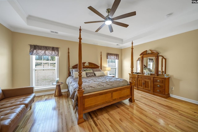 bedroom with multiple windows, light wood-type flooring, a raised ceiling, and visible vents