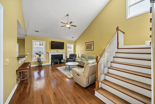 living area with a fireplace with flush hearth, ceiling fan, wood finished floors, high vaulted ceiling, and stairs