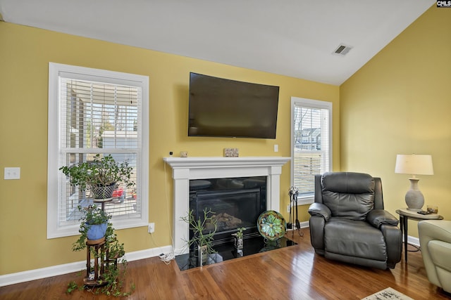 living room with a fireplace with flush hearth, wood finished floors, visible vents, vaulted ceiling, and baseboards