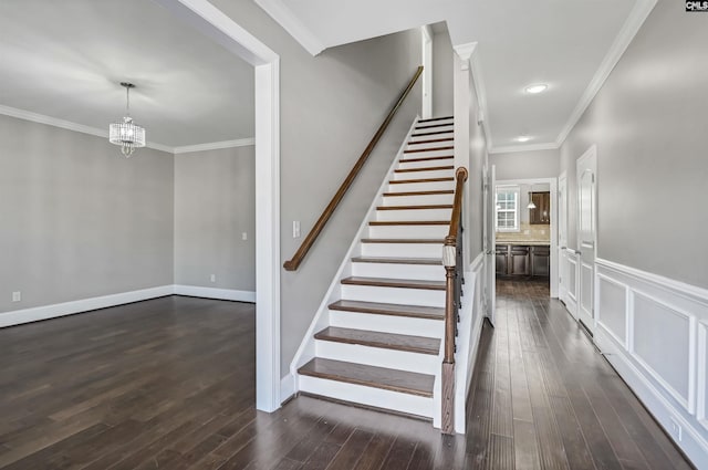 staircase featuring a chandelier, crown molding, baseboards, and wood finished floors