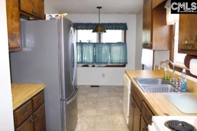 kitchen featuring a sink, wooden counters, freestanding refrigerator, brown cabinets, and decorative light fixtures