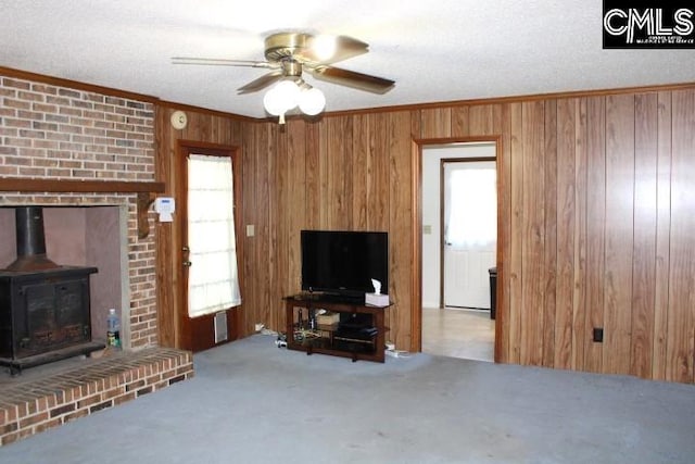 carpeted living room with a wood stove, wood walls, ceiling fan, and ornamental molding