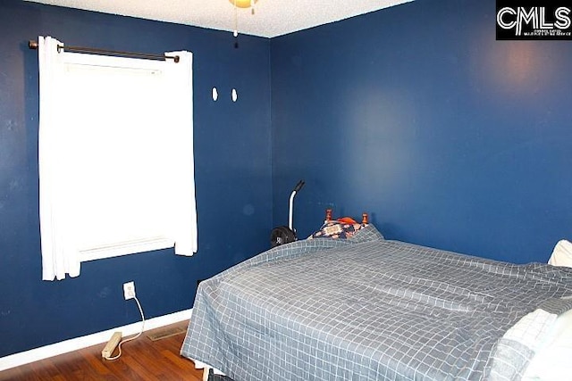 bedroom with a textured ceiling, baseboards, and wood finished floors