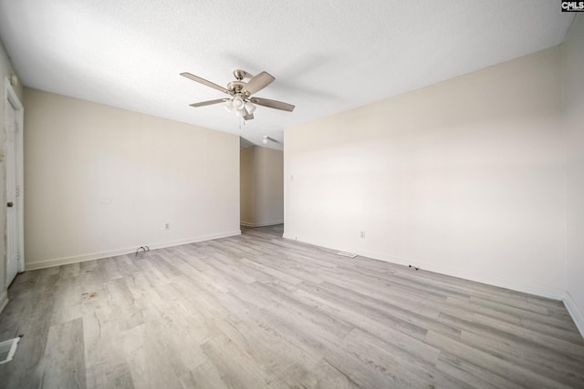 empty room with a textured ceiling, light wood finished floors, a ceiling fan, and baseboards