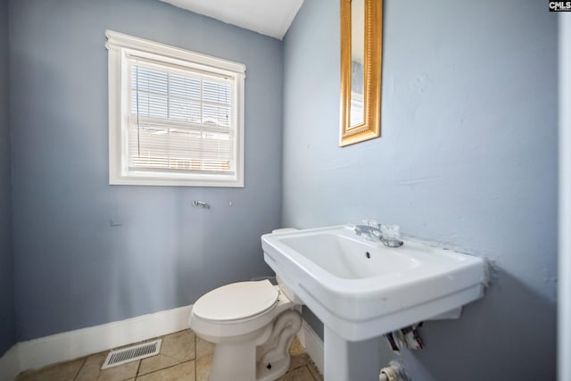 half bath with visible vents, toilet, a sink, tile patterned flooring, and baseboards