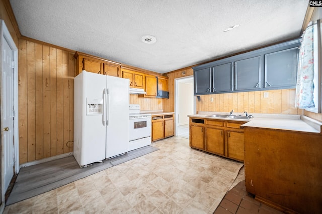 kitchen with light countertops, white appliances, wood walls, and a sink