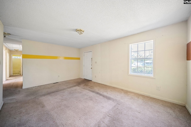 carpeted spare room with a textured ceiling, attic access, and baseboards