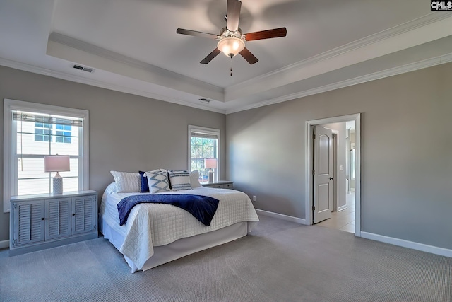 bedroom with light colored carpet, visible vents, baseboards, ornamental molding, and a raised ceiling