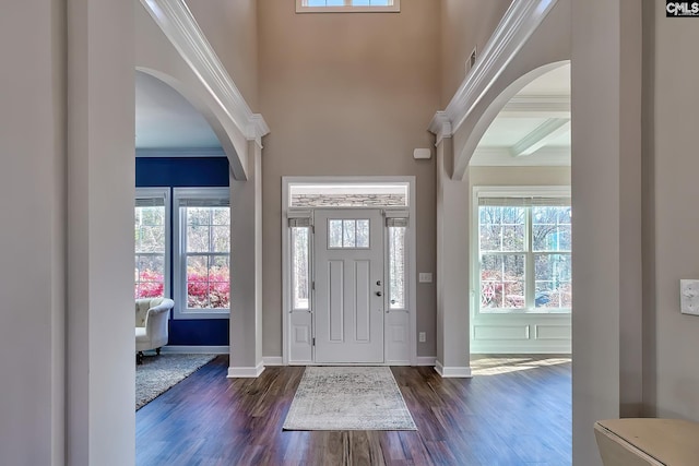 foyer with ornamental molding, arched walkways, and dark wood-style flooring