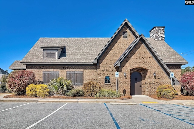 view of front of property featuring roof with shingles, uncovered parking, a chimney, and brick siding