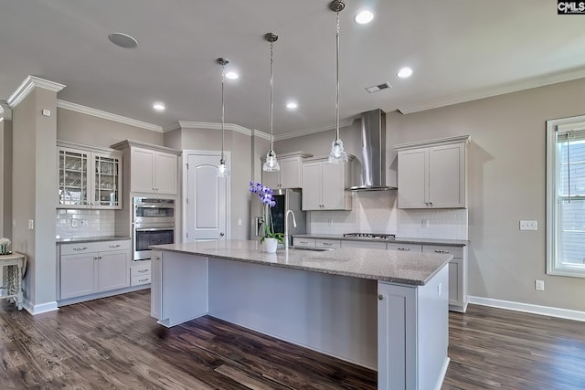 kitchen featuring visible vents, ornamental molding, a kitchen island with sink, a sink, and wall chimney range hood