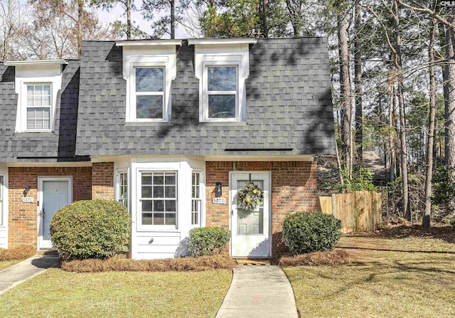 view of front of property featuring brick siding, mansard roof, and roof with shingles