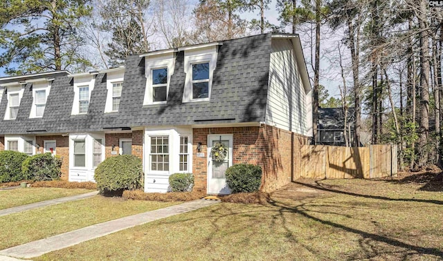 view of front of home with brick siding, fence, a front lawn, and roof with shingles