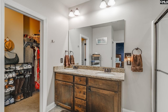 bathroom featuring double vanity, a sink, a walk in closet, and baseboards