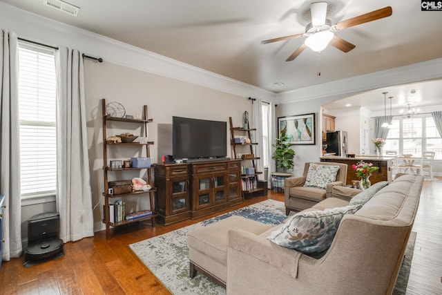 living room featuring wood-type flooring, visible vents, crown molding, and ceiling fan with notable chandelier