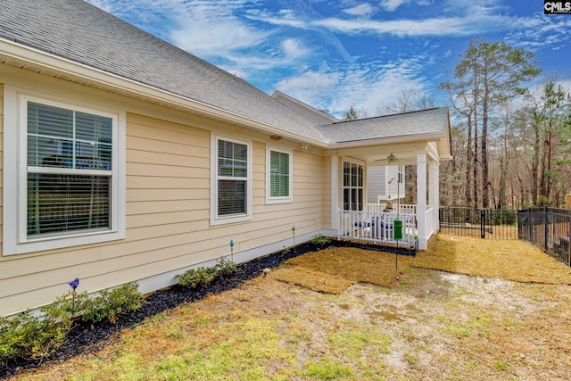 view of side of home featuring a shingled roof, fence, and ceiling fan