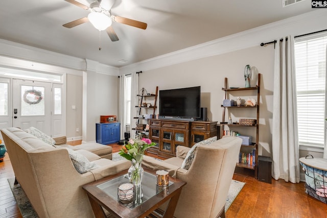 living room featuring ceiling fan, visible vents, baseboards, ornamental molding, and wood-type flooring