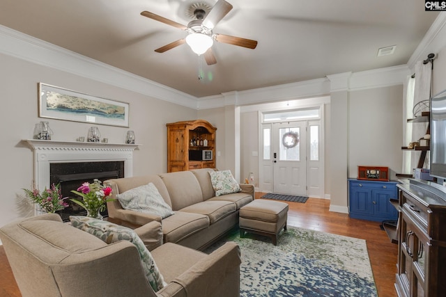 living room with ornamental molding, a fireplace, dark wood finished floors, and a ceiling fan